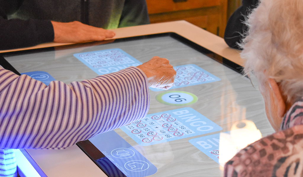 Ouderen spelen bingo op interactieve speeltafel met touchscreen
